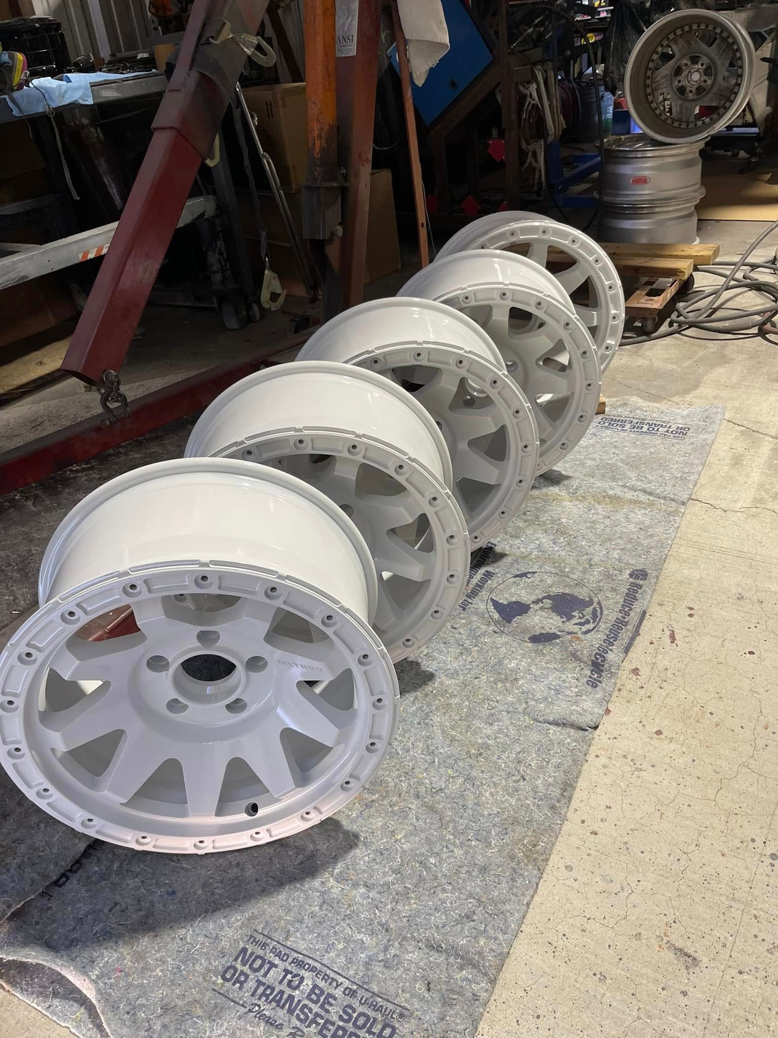 Five white powder coated off-road wheels lined up on the shop floor