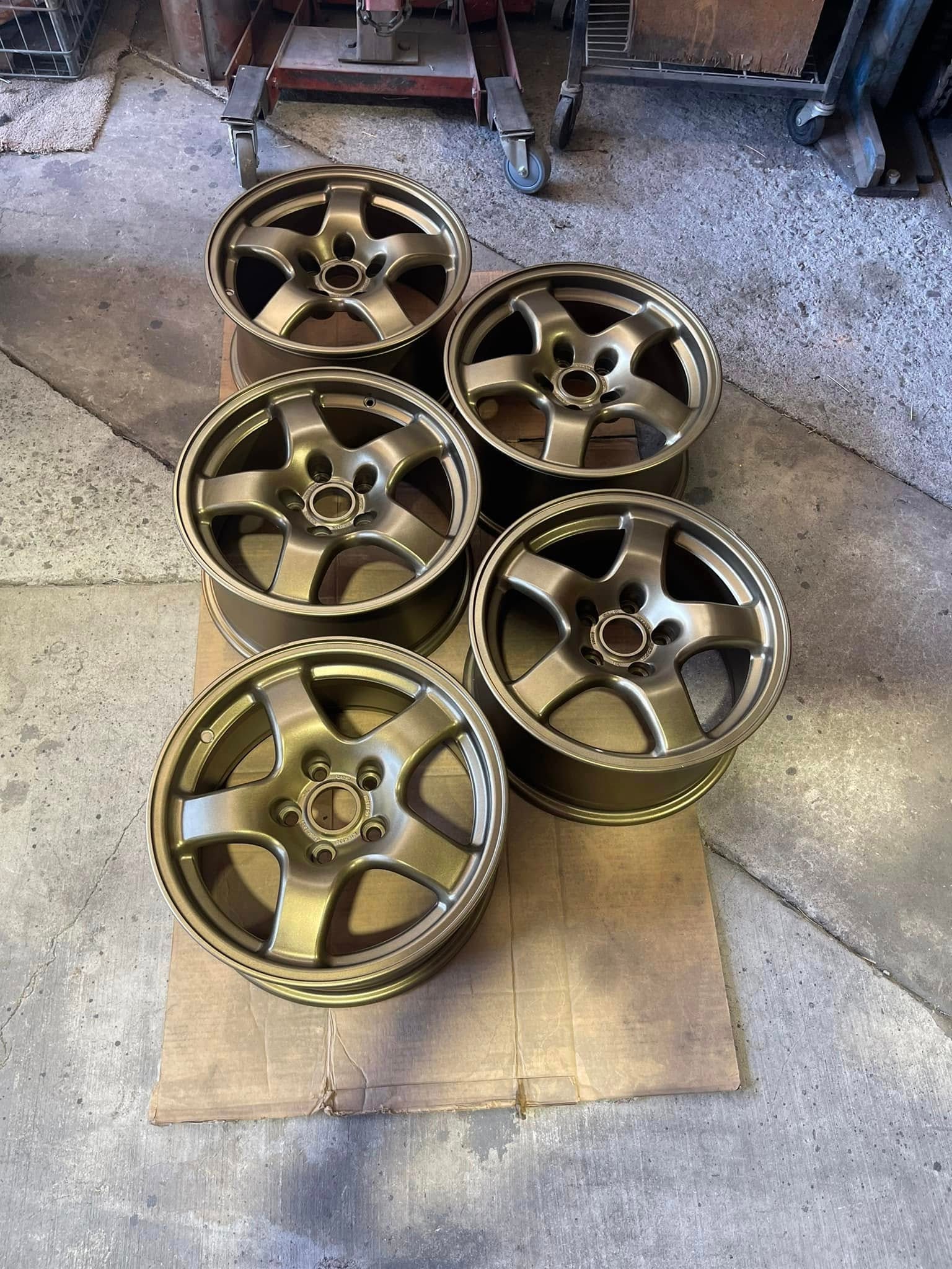 Five bronze powder coated alloy wheels laid out on cardboard