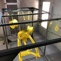 Yellow powder coated metal parts hanging in the paint booth