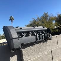 Textured black powder coated engine valve cover against a block wall