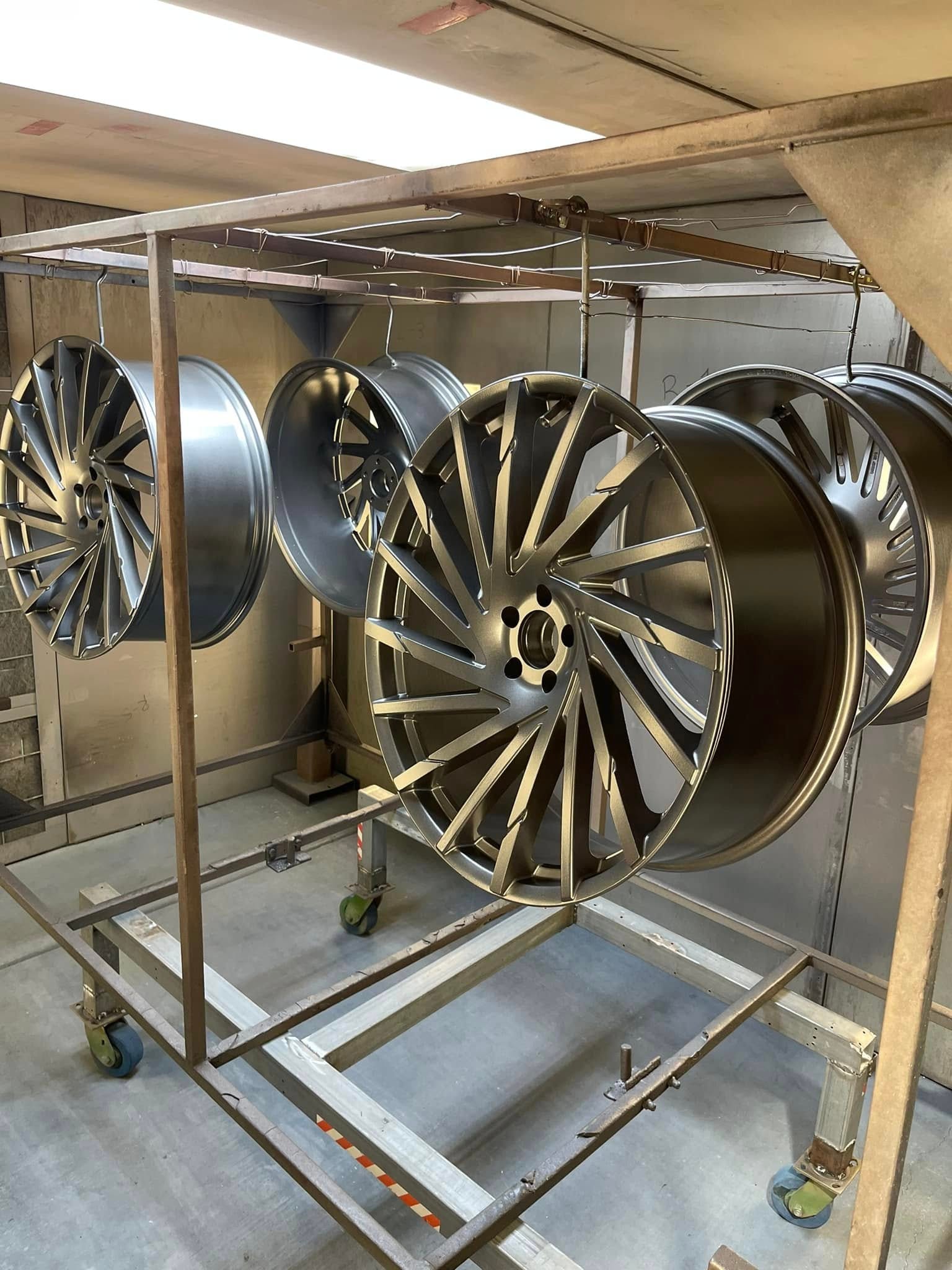 Gold multi-spoke wheels hanging in the powder coating booth
